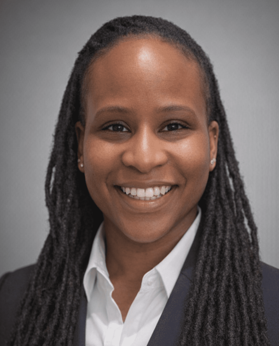 Portrait of a smiling woman with long dreadlocks wearing a white shirt and dark jacket.